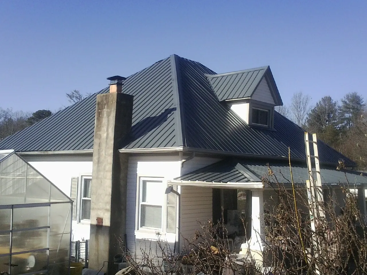 Dark blue standing seam metal roof on a white farmhouse with dormer — Slate & Tile Roof Repair by Roofing Brothers in Supply