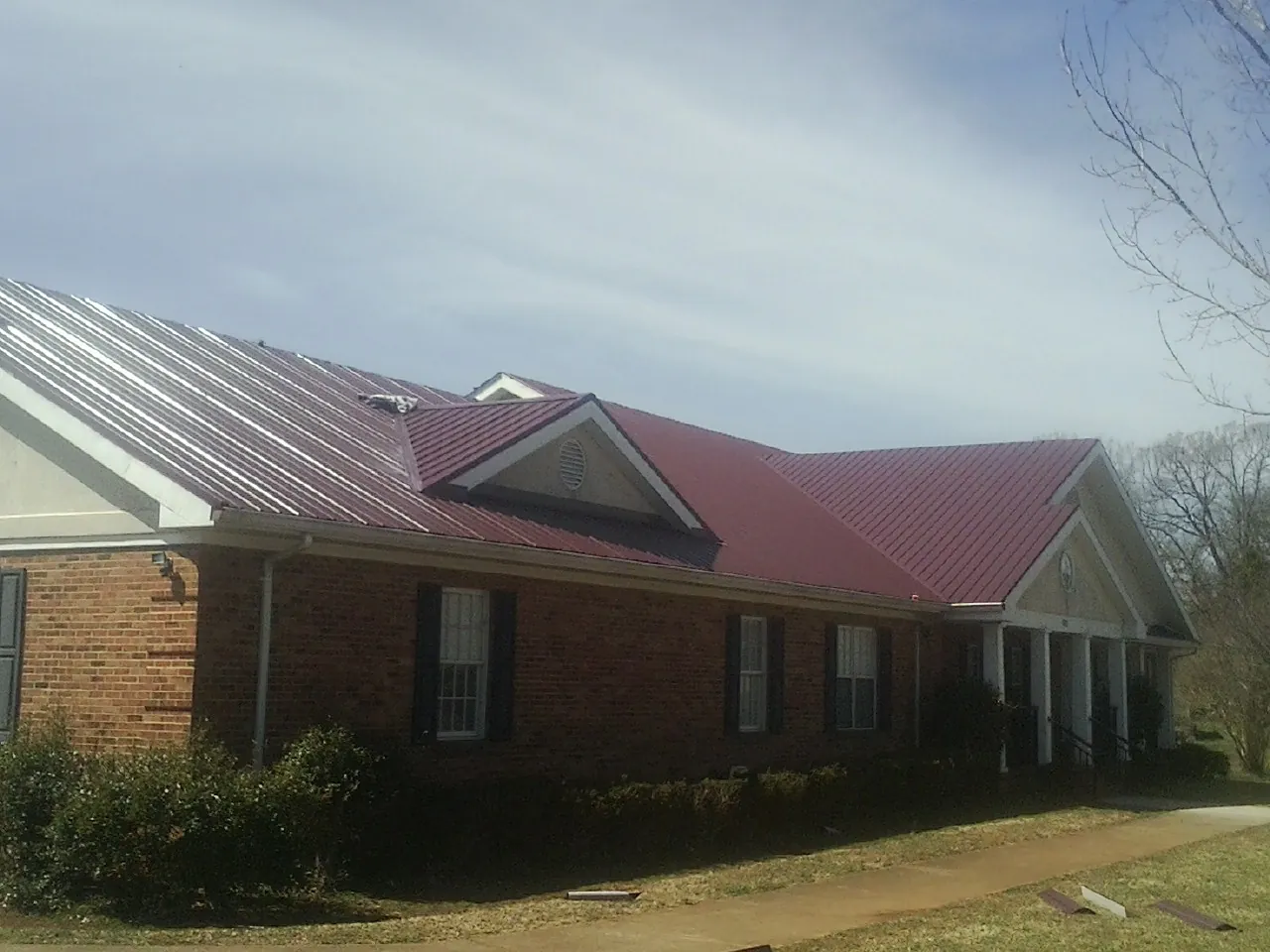 Red metal roof with gabled entries on a long brick building, from a Hail Damage Roof Repair job in Supply