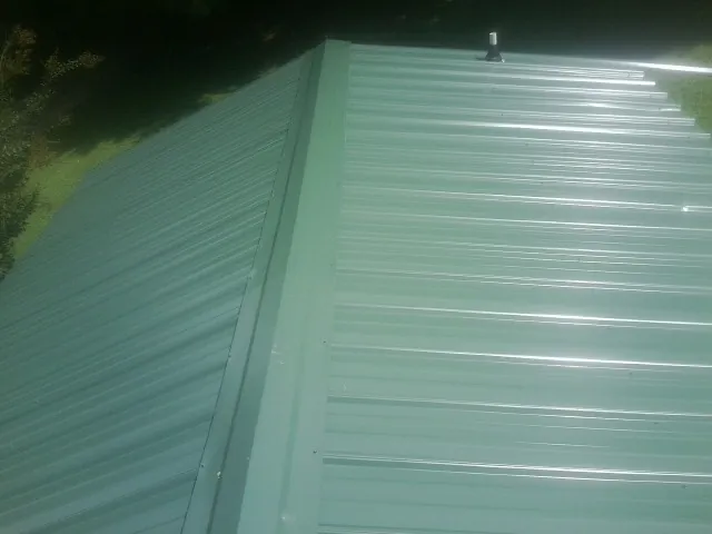 New green metal panels meeting at the ridge of a roof — Flat Roof Repair work by our crew in Supply