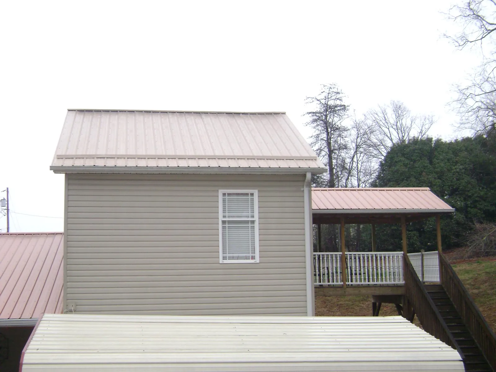 Tan metal roofs on a two story addition and attached porch, from a Roof Replacement job in Supply