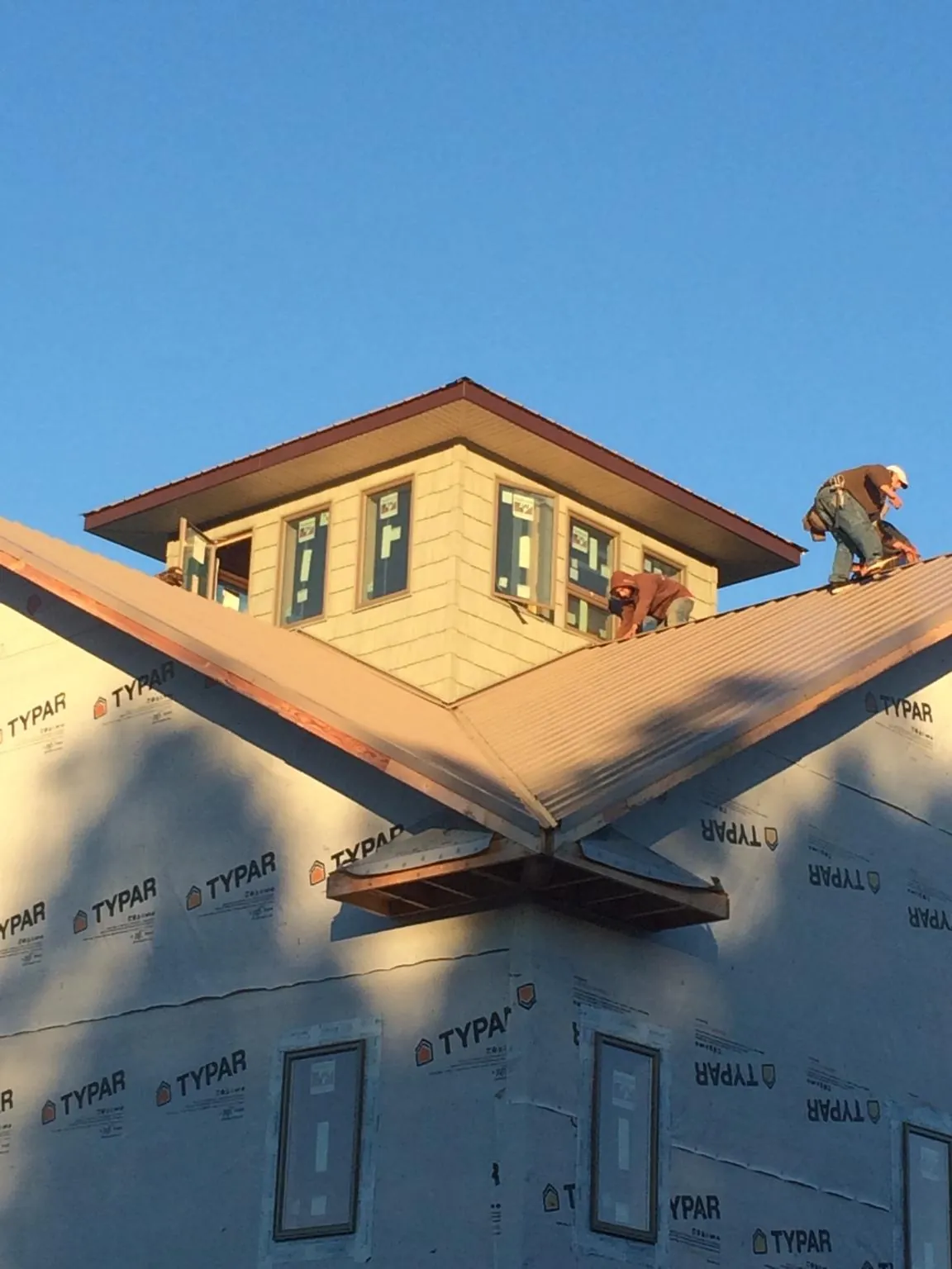 Roofers working around a rooftop cupola on a new metal roof at sunset — Roof Waterproofing in Supply by Roofing Brothers